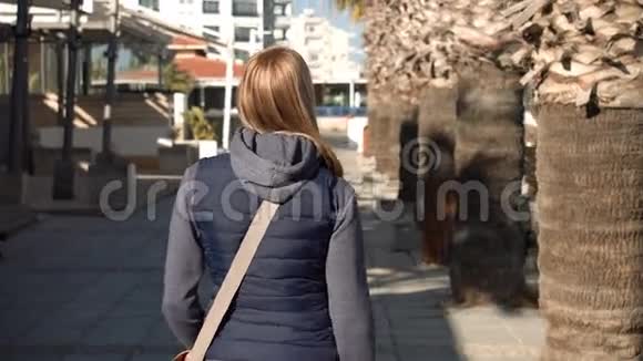 美丽迷人的女人走在街上阳光明媚从后面淡季度假村视频的预览图