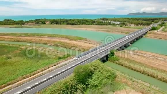空中飞行越过田野和桥河边在意大利托斯卡纳市之间的高速公路旁行驶的车辆视频的预览图