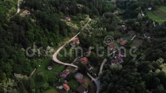 空中无人驾驶飞机在日落时分飞过被森林包围的东欧山村夏天绿树成荫视频的预览图