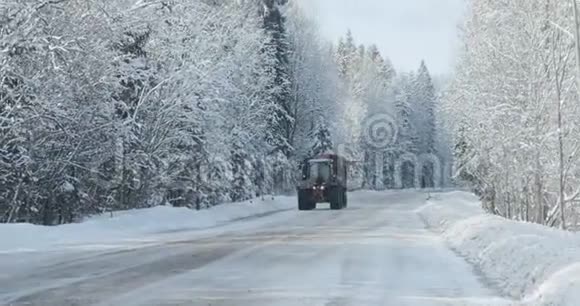 拖拉机正沿着森林附近的冬季道路行驶视频的预览图