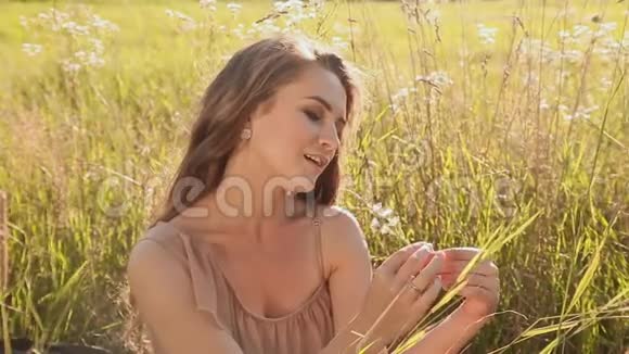 年轻漂亮的女孩坐在绿色的草地上她唱着那首捧花的歌特写镜头视频的预览图