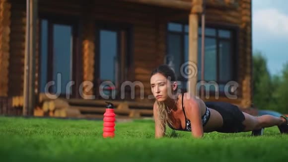 美丽的深色头发的女人在一个大房子的背景下从事健身和为新闻界做木板运动视频的预览图