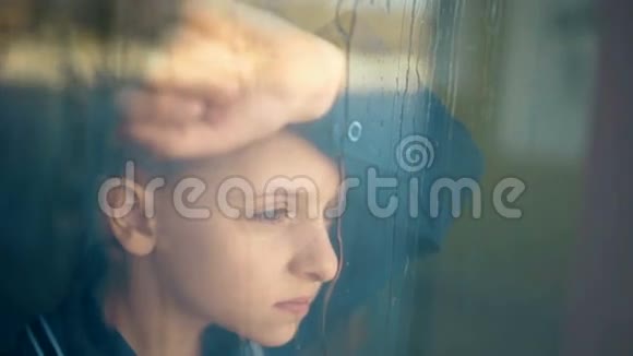 悲伤的不幸的孩子站在窗户附近窗外的雨视频的预览图