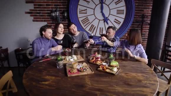 一群可爱的年轻人在一家现代化的的桌子上吃零食男人和女孩用酒杯烘焙视频的预览图
