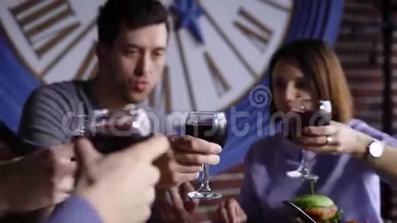 一群可爱的年轻人在一家现代化的的桌子上吃零食男人和女孩用酒杯烘焙视频的预览图