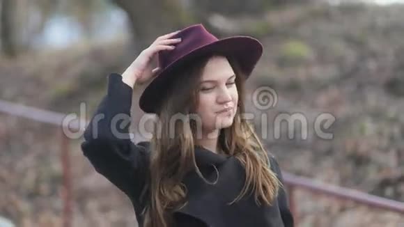 时尚开朗的年轻女孩留着长发紫色的帽子和黑色的外套走在街上多云多风天气视频的预览图