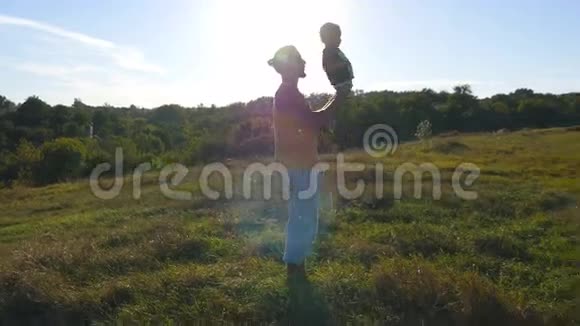年轻的父亲在大自然中和他的孩子玩耍爸爸抱着儿子腿把它扔到户外家庭幸福支出视频的预览图