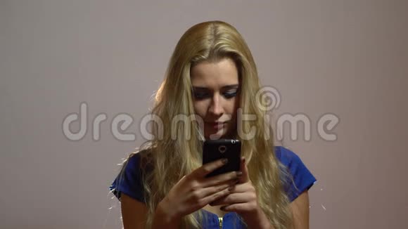 漂亮的金发女郎穿着蓝色礼服在工作室讲电话视频的预览图