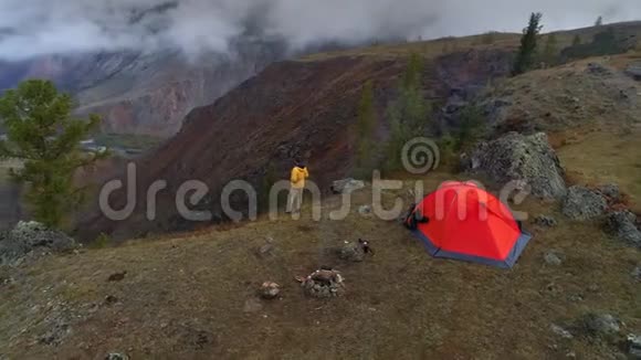 一名男子站在山谷前帐篷附近的空中镜头4K视频的预览图