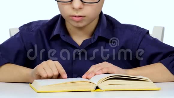 小男孩坐在桌子旁慢慢地读着有趣的书白色背景关门视频的预览图