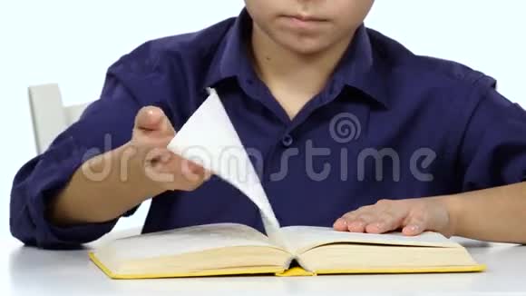 男孩坐在桌子旁翻阅一本书的页数白色背景关门视频的预览图