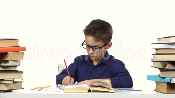男孩坐在一张桌子旁在她的笔记本上记录了一些东西然后翻了翻书白色背景视频的预览图