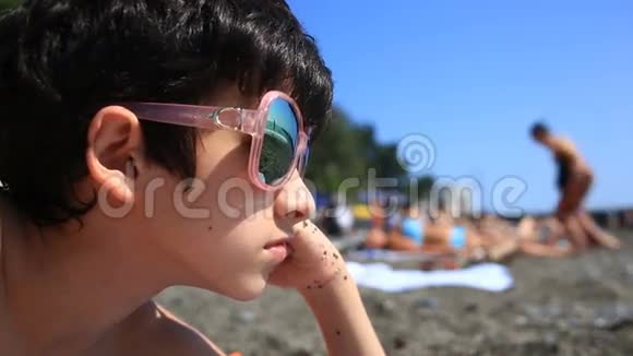 男孩是一个十几岁的孩子在海滩上戴着太阳镜海滩上有度假者戴着眼镜粉色眼镜视频的预览图