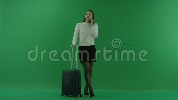 女孩站在手提箱旁边在绿色屏幕上打电话视频的预览图
