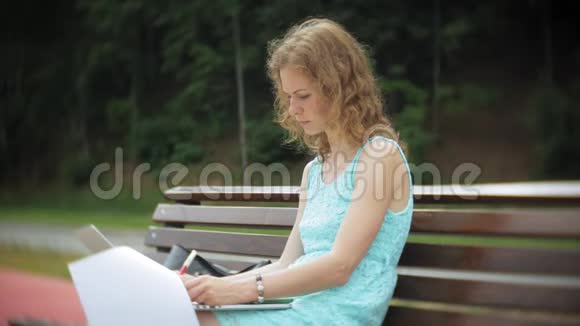 一个女人坐在沙滩上的长凳上在阅读文件中享受着笔记本电脑视频的预览图