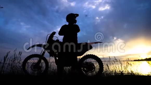 一个骑摩托车的人站在他的车旁边的轮廓一个在日落背景下的人坐在他的车上是视频的预览图