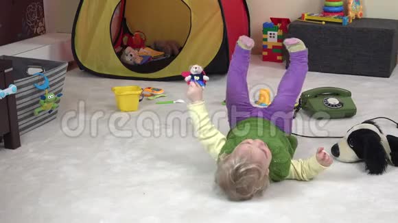 小可爱的女孩躺在她房间里玩具之间的白色地毯上4K视频的预览图