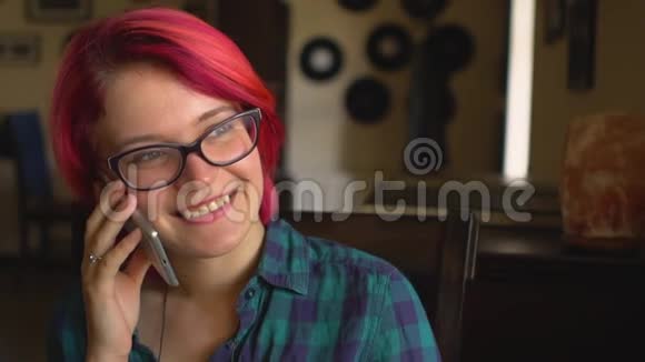 年轻漂亮的女人红头发嘴唇用银色的智能手机说话看着咖啡馆里的窗户视频的预览图