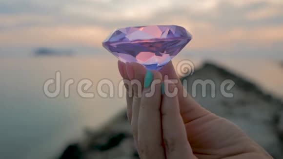 紫色钻石水晶在女性手中特写在夕阳的背景下视频的预览图
