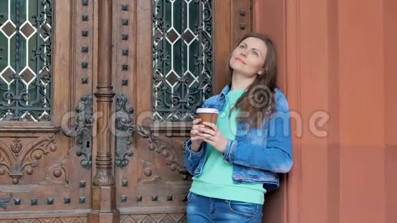 穿着棉袄喝咖啡的漂亮女孩背景中的老式建筑视频的预览图