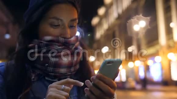 年轻的混血时髦女孩在圣彼得堡的夜晚街头使用手机4K慢动作俄罗斯视频的预览图