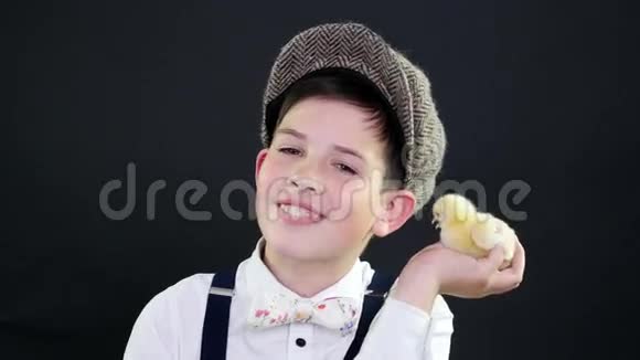 肖像一个戴着帽子和吊带的漂亮男孩和一只黄色的小鸭子玩专题装饰的工作室视频视频的预览图