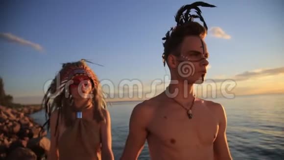 美丽的美国土著男女穿着传统服装日落时漫步在海边视频的预览图
