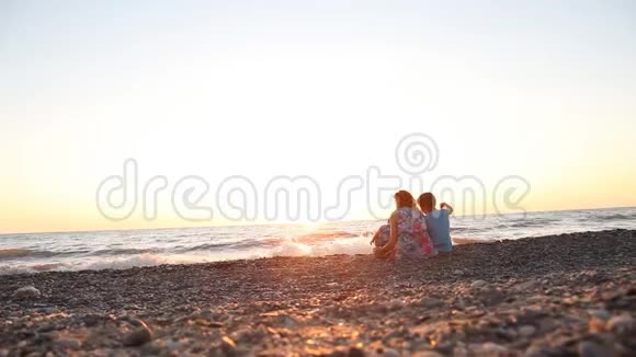 妈妈和两个男孩日落时在海边的海滩上休息视频的预览图