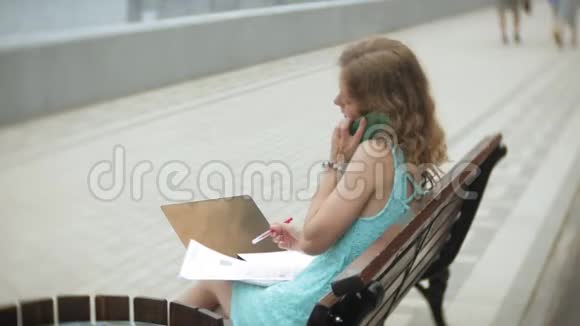 一个女人坐在沙滩上的长凳上在阅读文件中享受着笔记本电脑视频的预览图
