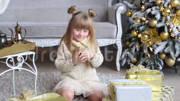 情绪激动的小女孩手里拿着一个礼盒试着在家的圣诞树附近打开视频的预览图