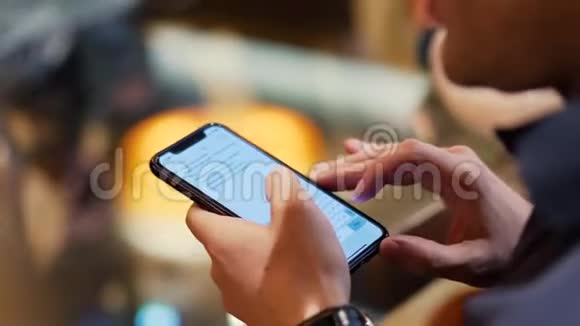年轻时髦的家伙在酒吧用手机发短信库存一个年轻人手里拿着电话在咖啡馆里视频的预览图