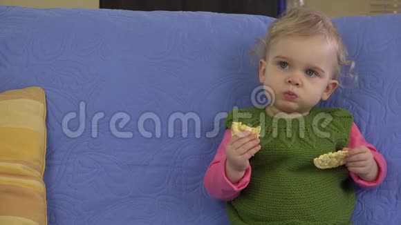 可爱的女婴在房间里坐在蓝色沙发上吃饼干4K视频的预览图