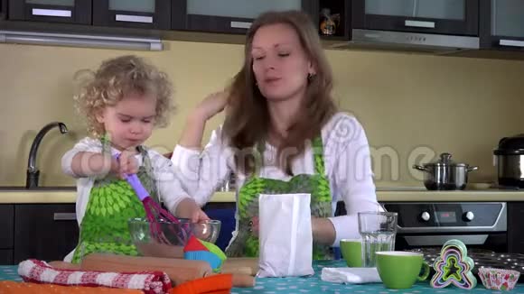 可爱的女孩和妈妈在厨房的桌子上的玻璃碗里混合巧克力粉视频的预览图