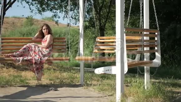 美丽的少女坐在夏日公园的长椅上视频的预览图