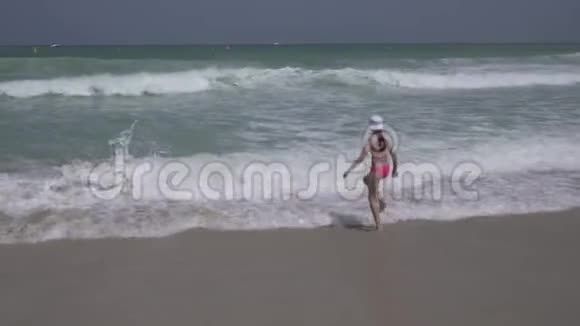 穿着泳衣的少女在迪拜海滩上快乐地跳进波斯湾的海浪中视频的预览图