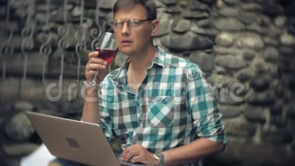 一个在石墙背景上拿着笔记本电脑和文件的男人在工作喝着杯子里的酒视频的预览图