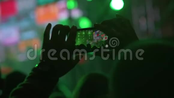 手在人群中拿着智能手机和拍摄音乐表演舞台上明亮的灯光视频的预览图