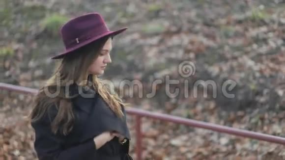 美丽的年轻女孩走在公园里长发秋装戴着帽子侧视慢镜头视频的预览图