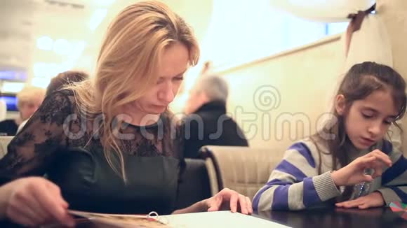 带着女儿在咖啡馆的女人女人在咖啡馆里看菜单视频的预览图