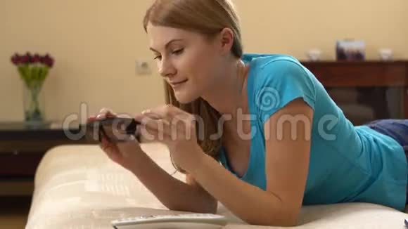 美丽迷人的年轻女子穿着蓝色t恤躺在沙发上穿着3D眼镜看电视视频的预览图
