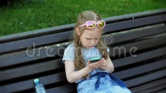 小女孩坐在城市的木凳上使用智能手机城市公园背景视频的预览图