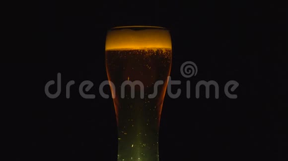 一杯啤酒慢慢地绕着它的轴转关闭4K视频黑色背景视频的预览图