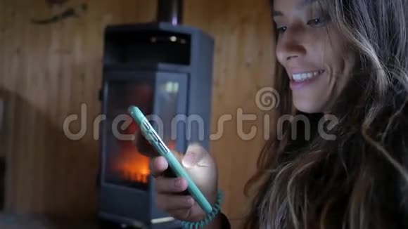 一个年轻迷人的混合种族妇女微笑和使用移动电话在壁炉附近的肖像科技高清视频的预览图
