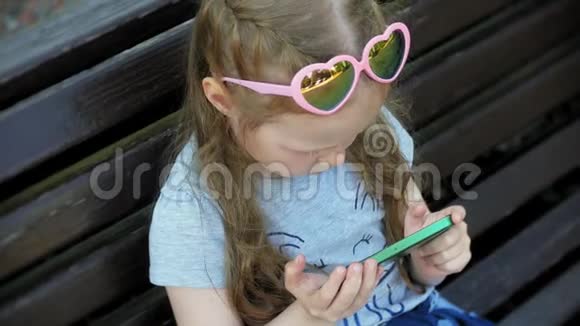 小女孩坐在城市的木凳上使用智能手机城市公园背景视频的预览图