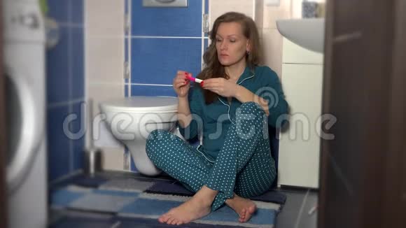 女人坐在浴室里拿着两条条纹的妊娠试验视频的预览图