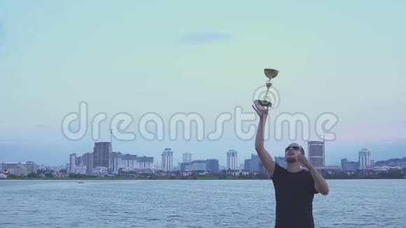 一个手里拿着杯子的年轻人为体育胜利而高兴舞蹈和跳跃在晚城胜利的概念视频的预览图