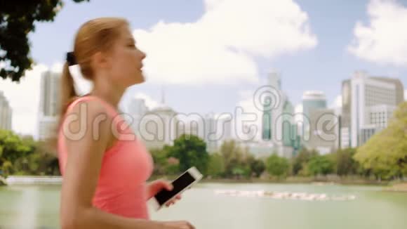 女子跑步者在公园慢跑适合女性运动健身训练在她的智能手机上自拍视频的预览图