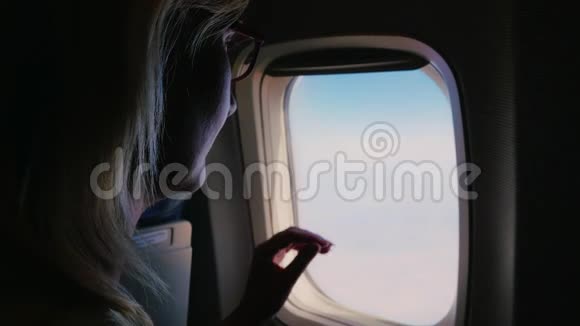一个年轻的女人关上一扇飞机窗户看着窗外黑暗的框架被照亮的开口视频的预览图