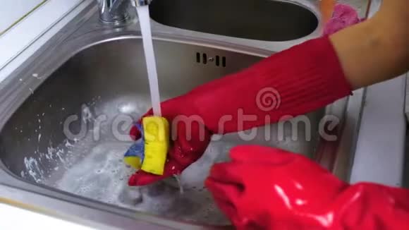 女人用红色手套在厨房里洗了一个带海绵的金属水龙头双手特写视频的预览图