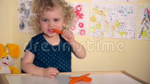 有趣的蹒跚学步的女孩坐在她房间的桌子旁吃胡萝卜视频的预览图